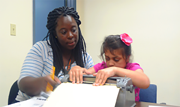 Teacher assisting young girl with Braille.